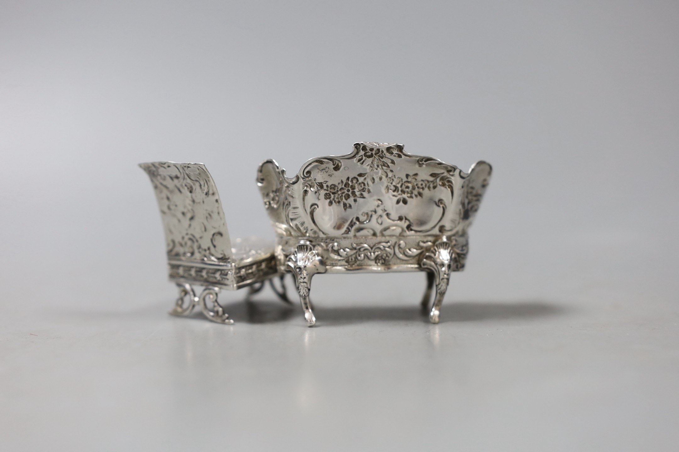 An Edwardian silver miniature model of a two seater settee, import marks for Elly Isaac Miller, London, 1902, width 68mm and a similar model of a chair, import marks for Eustace George Parker, London, 1897.